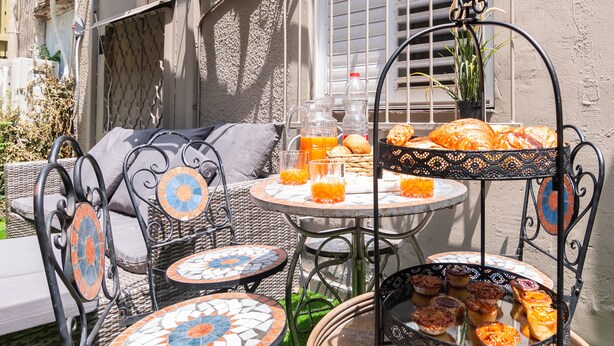 A patio with wicker furniture, a mosaic table, and a hanging basket with pastries. - Chateau Tel Aviv (Tel Aviv)
