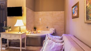 A bathroom with a bathtub, a vanity with a mirror, a television mounted on the wall, and a couch with pillows. - Chateau Tel Aviv (Tel Aviv)