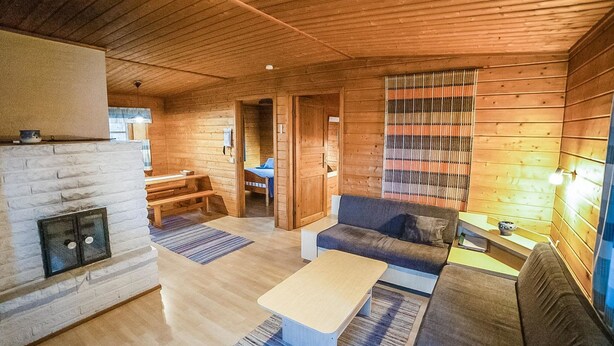 Un acogedor interior de cabaña con chimenea, paredes de madera, un sofá, una mesa de comedor y una cama.