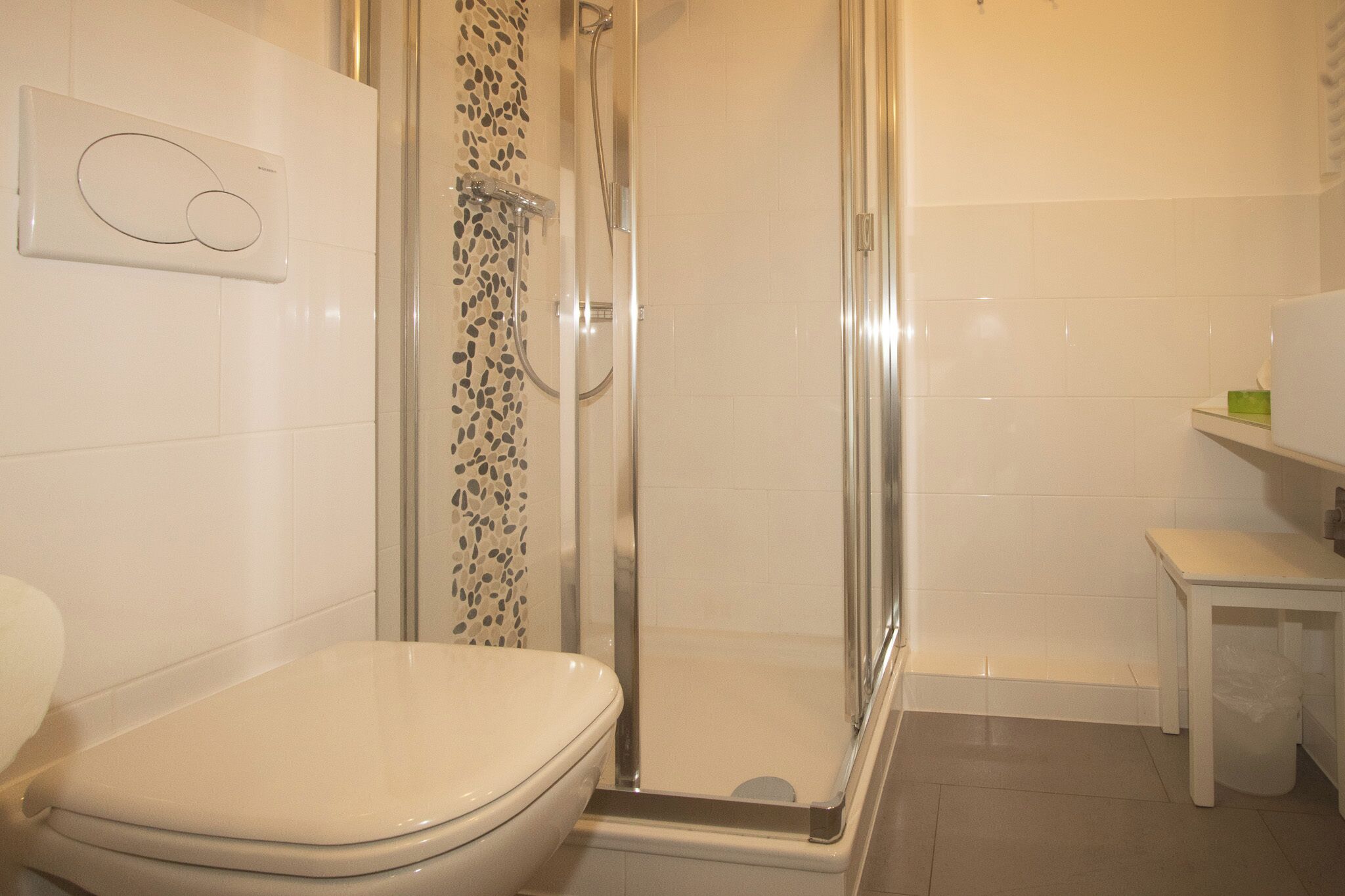 Un baño con inodoro, ducha y una pequeña mesa con un cubo de basura.