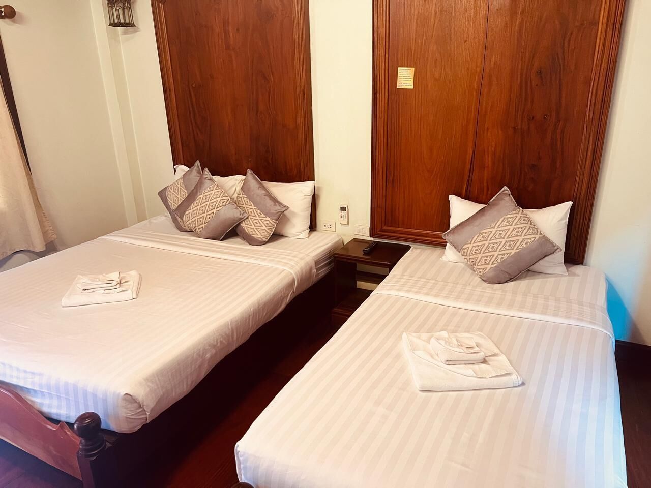 Two single beds with wooden headboards, each with a pillow and a folded towel on the bed.
