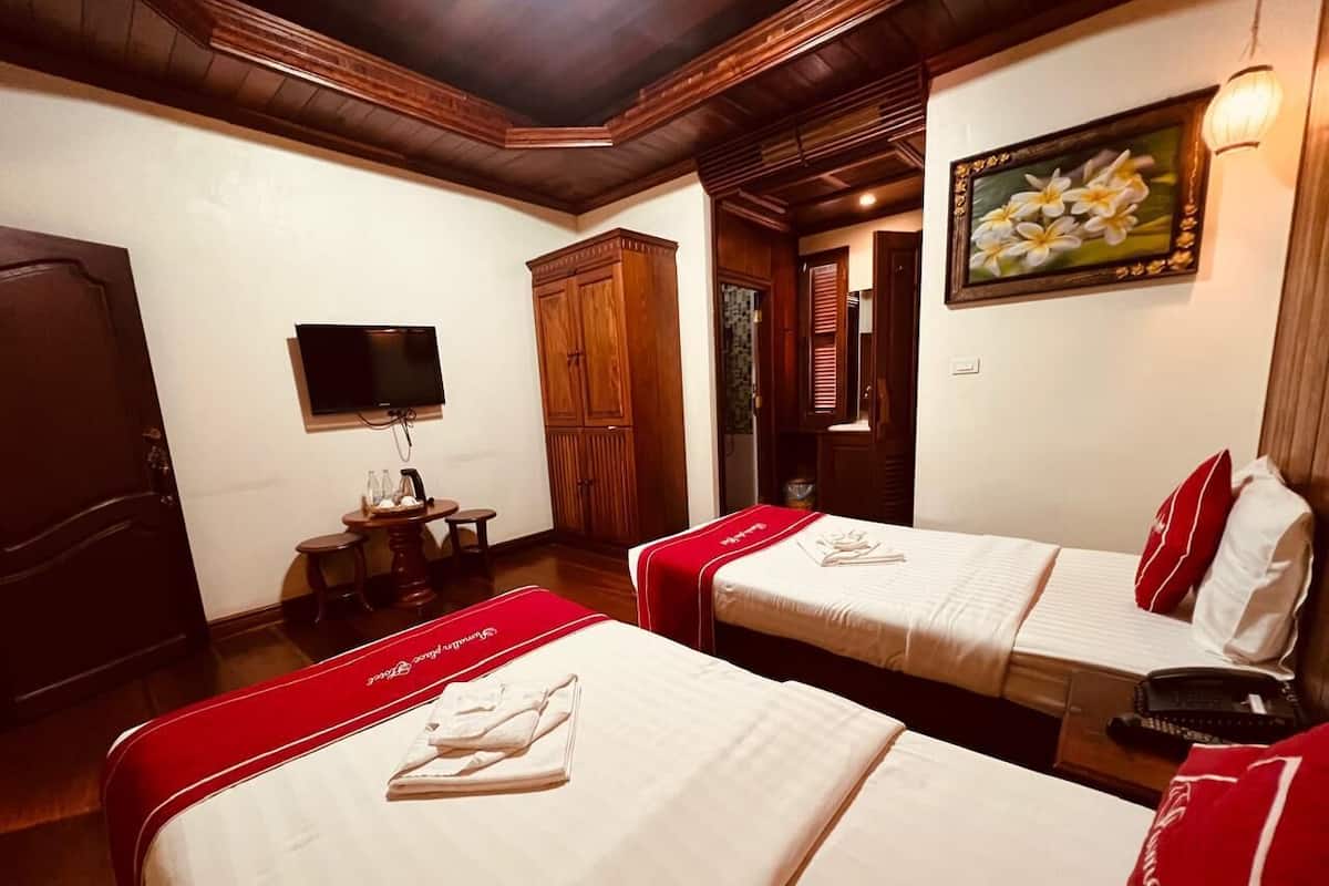 A hotel room with two beds, a TV, a wooden wardrobe, and a painting on the wall.