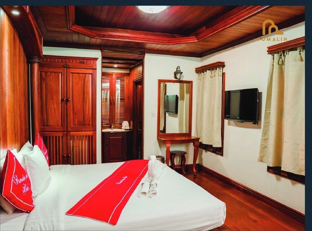 Ein Hotelzimmer mit Holzboden, einem Bett mit roter Bettdecke, einem Fernseher, einem Spiegel und einem Fenster mit Vorhängen.