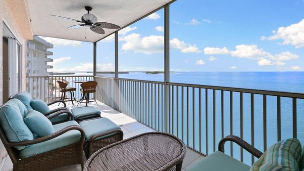 Un balcone con mobili in vimini, una ventola a soffitto e vista sull'oceano.