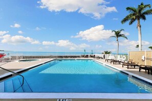 A swimming pool with a 3 FT depth marker, surrounded by lounge chairs and palm trees, with a view of the ocean. - Dela Park Place - Waterfront 2BDR/2BA with Den (Marco Island)