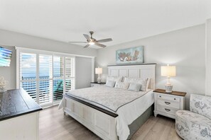 A bedroom with a large bed, a ceiling fan, a nightstand with a lamp, and a view through a sliding door. - Dela Park Place - Waterfront 2BDR/2BA with Den (Marco Island)