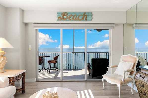 A room with a view of the sea, a 'Beach' sign, a table with chairs, and a white armchair. - Dela Park Place - Waterfront 2BDR/2BA with Den (Marco Island)
