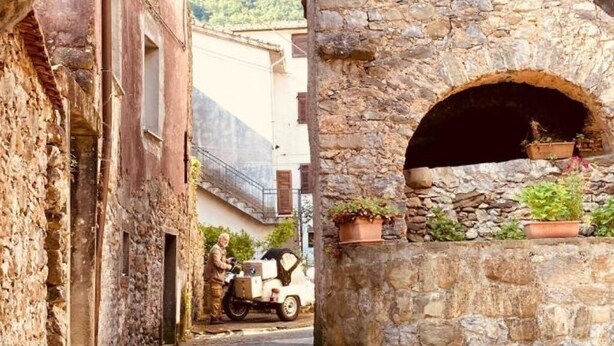 Una calle estrecha con edificios de piedra, un arco de piedra con una planta en maceta y una motocicleta estacionada.