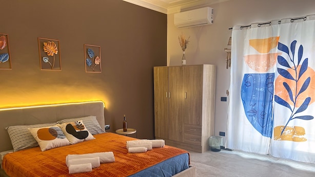 Una cama bien hecha con una colcha azul y naranja, un armario de madera y un aire acondicionado de pared.