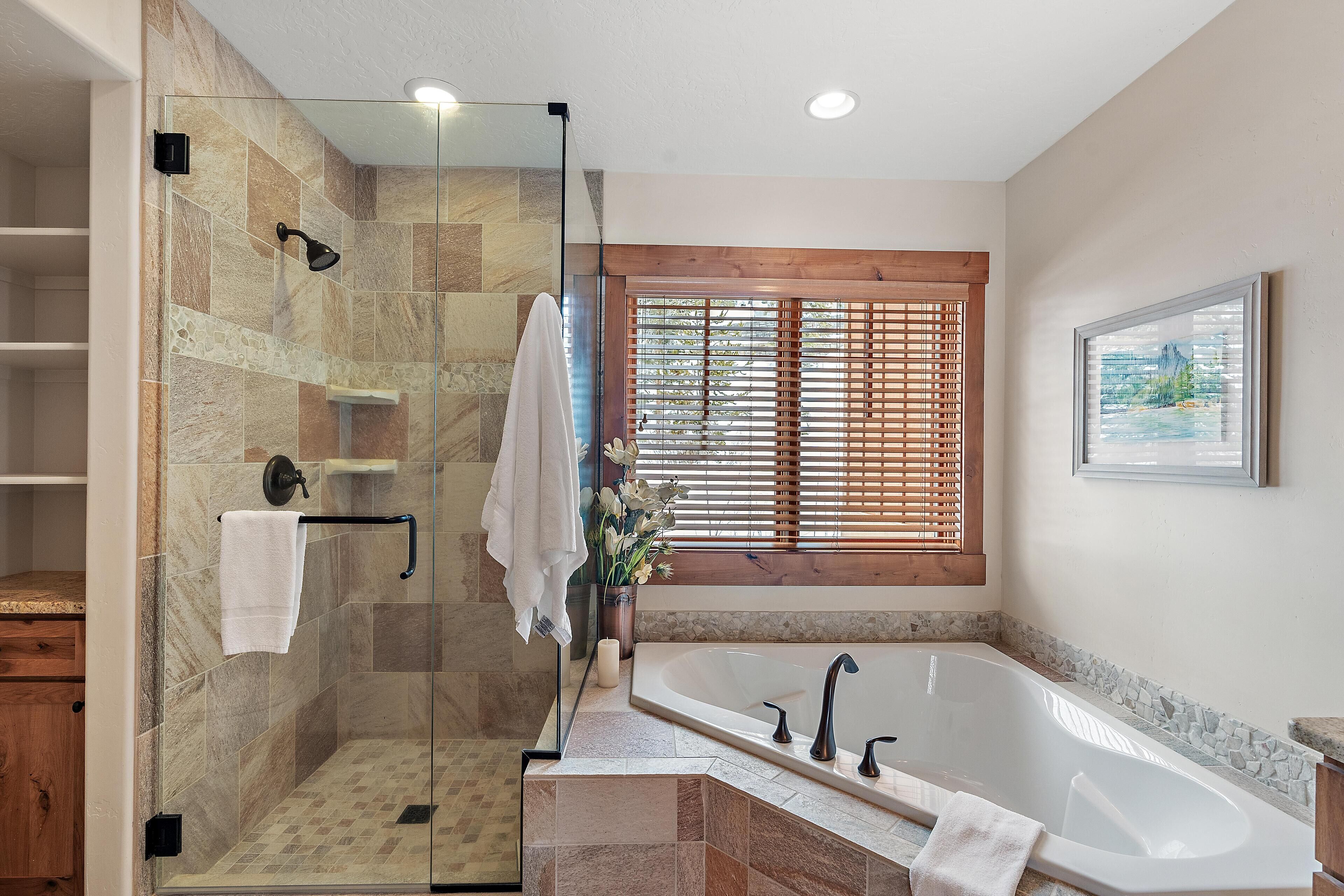 Une salle de bain moderne dotée d’une douche à parois de verre, d’une baignoire sur pieds et d’une fenêtre avec des stores en bois.