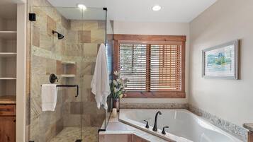 Une salle de bain moderne dotée d’une douche à parois de verre, d’une baignoire sur pieds et d’une fenêtre avec des stores en bois.