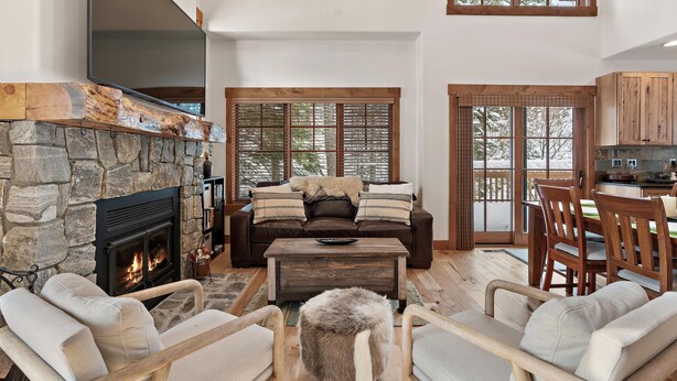 A cozy living room with a stone fireplace, a leather sofa, and a dining area with wooden chairs and a table.
