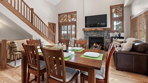 A spacious living area with a wooden staircase, a fireplace, and a dining table set with plates and candles.