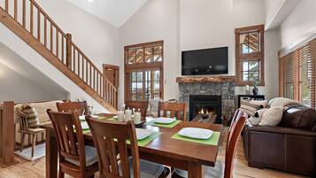 A spacious living area with a wooden staircase, a fireplace, and a dining table set with plates and candles.
