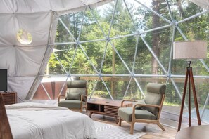 Une pièce aménagée avec une tente, un lit, deux chaises, une table et une lampe.