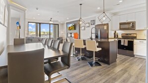 Una cocina moderna con electrodomésticos de acero inoxidable, un comedor con una mesa larga y sillas, y un amplio ventanal con vistas al exterior.