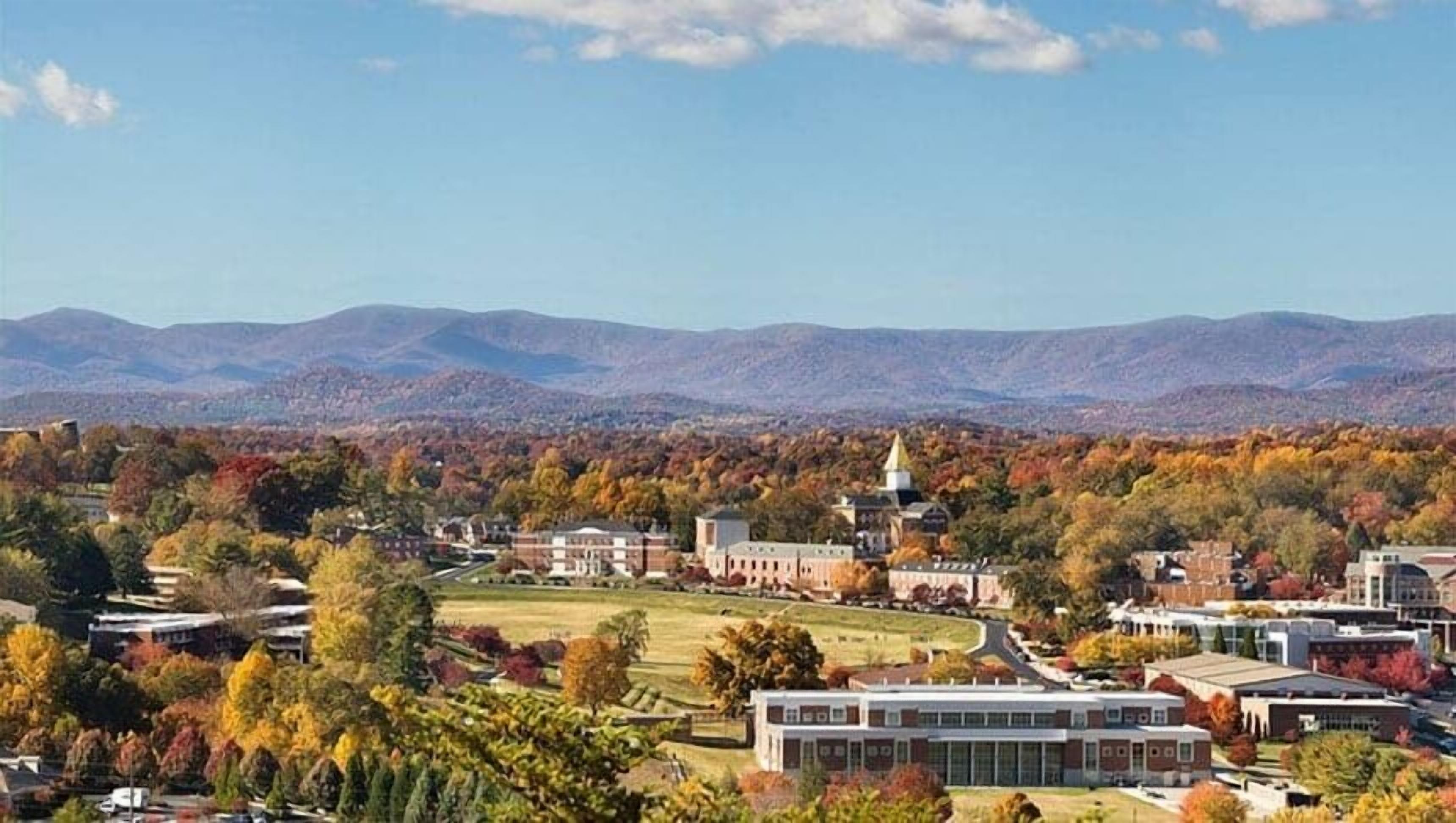 A campus with buildings, a prominent clock tower, and a mountainous backdrop.