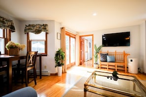 A living room with a wooden dining table, chairs, a sofa, a TV, and a coffee table.