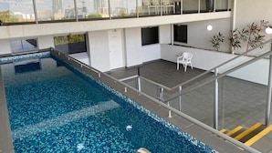 An indoor swimming pool with a glass balustrade, a seating area with chairs, and a view of the cityscape through the windows. - Katara on Smith (Darwin)