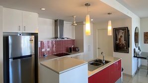 A modern kitchen with white cabinets, a stainless steel refrigerator, a red and white tiled backsplash, pendant lights, and a painting on the wall. - Katara on Smith (Darwin)