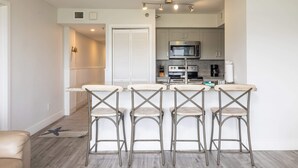 Una cocina moderna con electrodomésticos de acero inoxidable, una barra con cuatro taburetes y piso de madera.