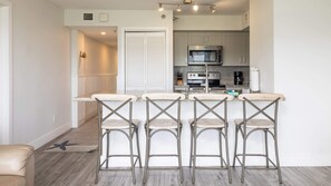 A modern kitchen with stainless steel appliances, a bar area with four stools, and a wooden floor. - Nauti Hideaway Ocean Pointe 2314 (Tavernier)