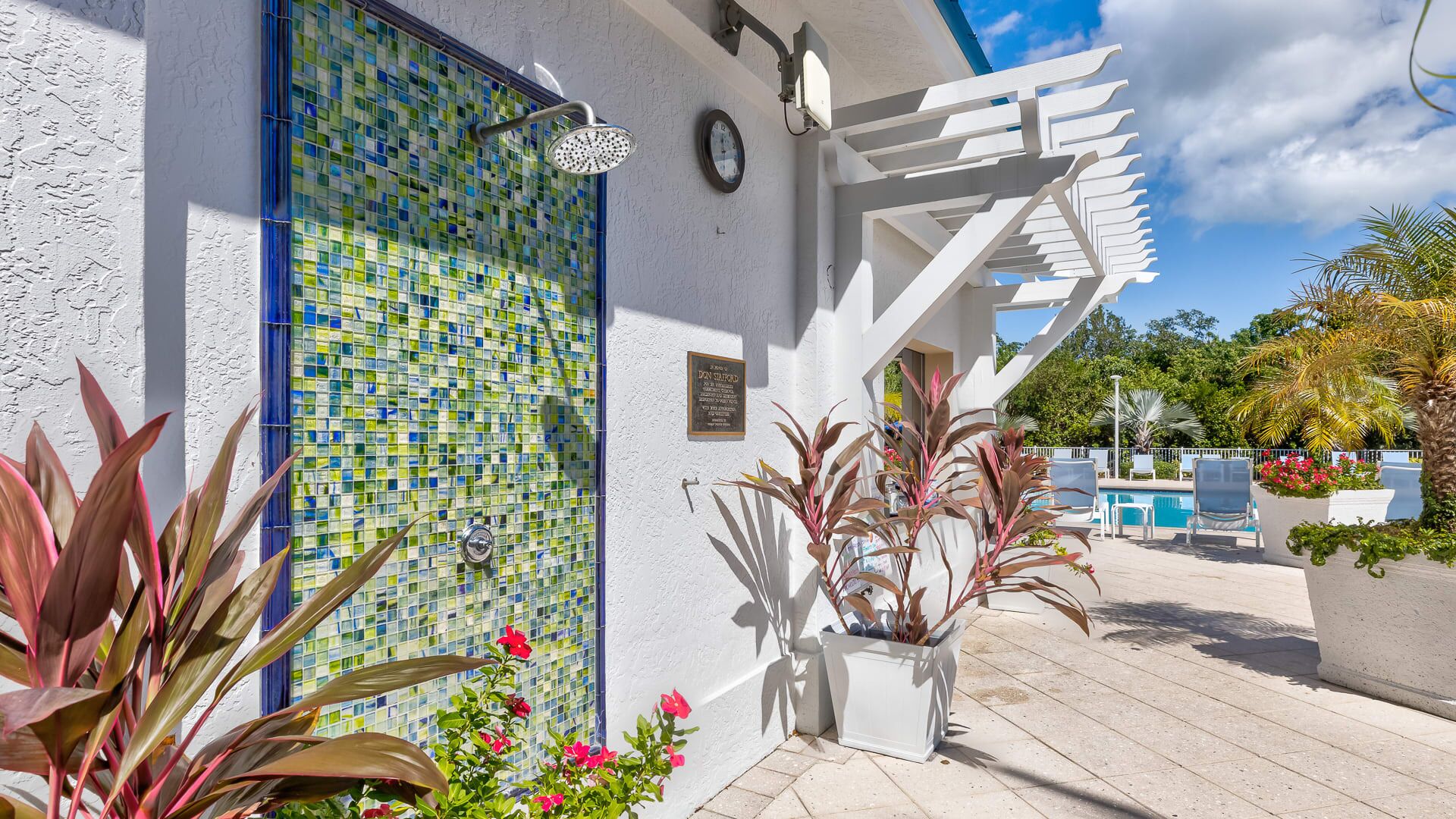 A modern building with a mosaic-tiled wall, a white pergola, and a pool area with lounge chairs.