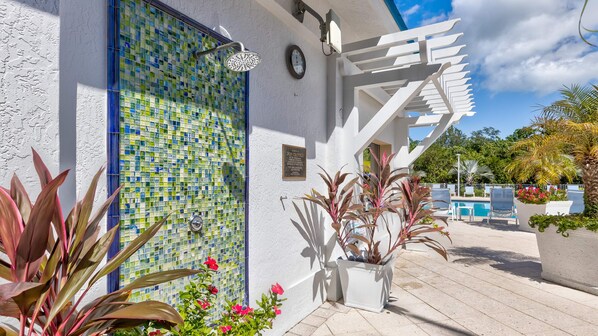 A modern building with a mosaic-tiled wall, a white pergola, and a pool area with lounge chairs.