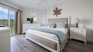 Un dormitorio con una cama grande, una mesita de noche con lámpara, cómoda, espejo y vistas al exterior.