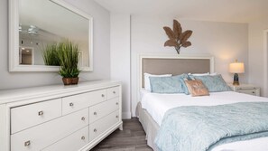 A bedroom with a bed, a dresser, a mirror, a potted plant, and a wall-mounted decorative leaf.