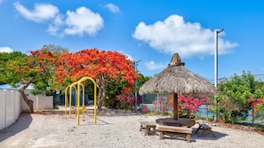 A playground with yellow swings, a thatched-roof structure, and benches.