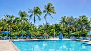 A swimming pool with lounge chairs and umbrellas, surrounded by palm trees.