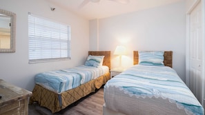A double room with two beds, a bedside table with a lamp, a window with blinds, and a mirror on the wall.