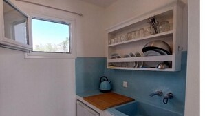 Una cucina compatta con una finestra, un lavello e mensole sopra per stoviglie.