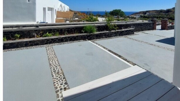 Una terrazza sul tetto con un cordolo in pietra, un edificio bianco e un cielo azzurro limpido.