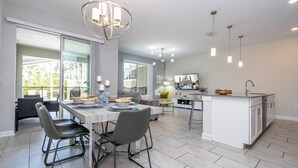 A modern kitchen with a central island, dining area with chairs, and a large window providing natural light. - Modern 4Bed+PrivatePool Resort Style 8959 (Davenport)