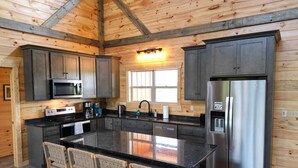 A modern kitchen with wooden walls, a central island, and stainless steel appliances. - Maple Moon | Hot tub | WiFi | New | Views (Rogers)