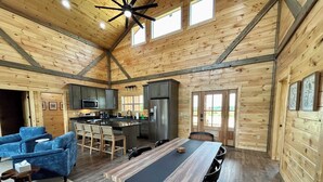 A spacious cabin interior with a wooden interior, a dining area, kitchen, and a seating area with blue chairs. - Maple Moon | Hot tub | WiFi | New | Views (Rogers)