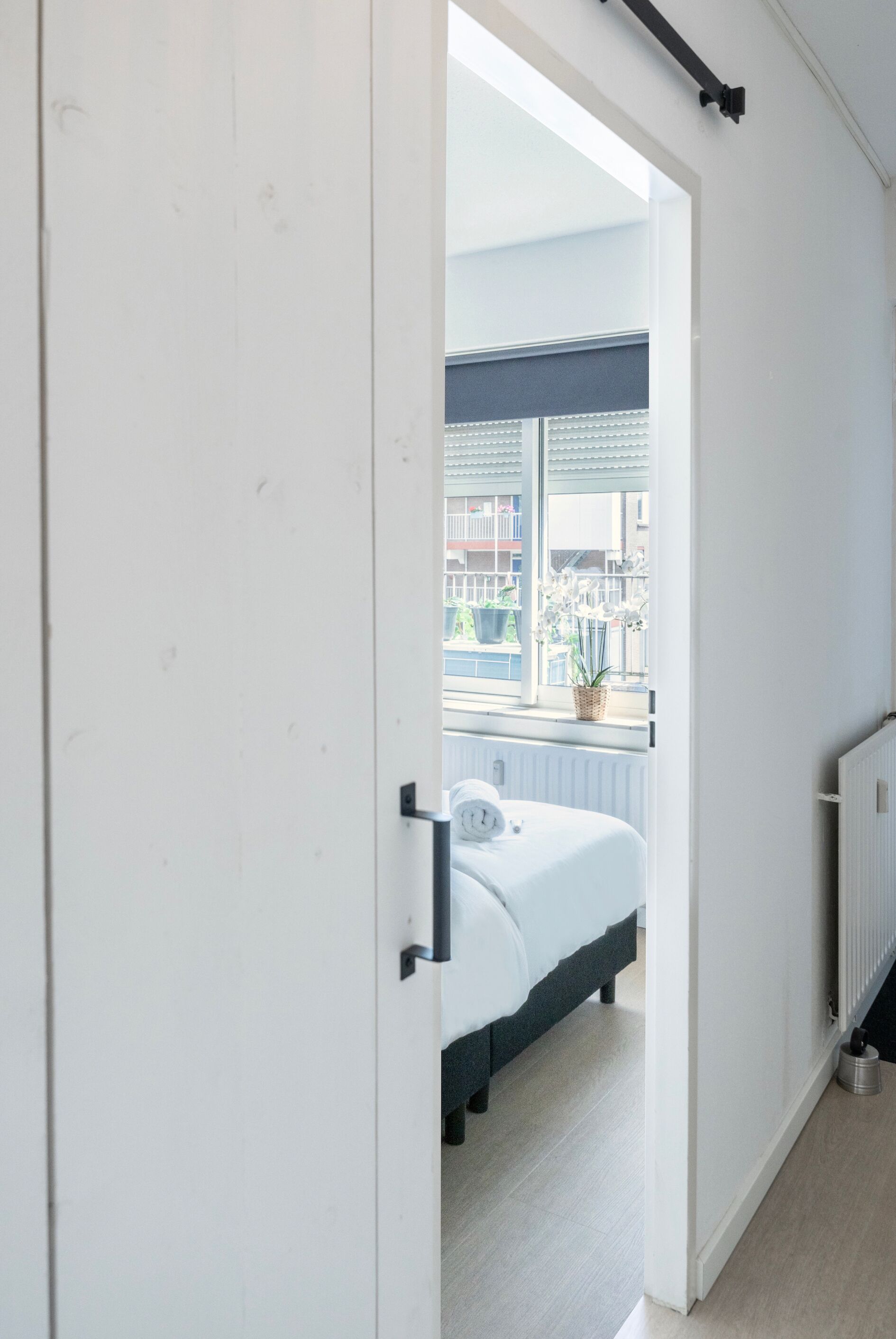 A bedroom with a bed, a radiator, and a window with a view of buildings and greenery.
