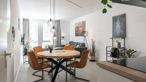 Ett modernt vardagsrum med ett runt matbord, soffor och ett soffbord. Det finns växter, en bokhylla och konstverk på väggarna.