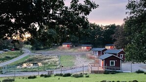 Entorno rural con varias cabañas de madera, un camino de tierra y una zona cubierta de césped.