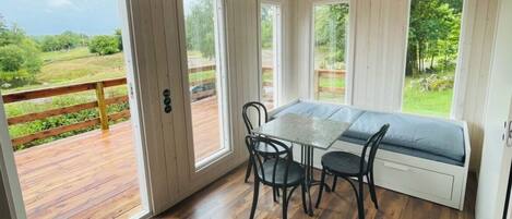 Une pièce avec une terrasse en bois, une table et deux chaises, ainsi qu’un banc doté d’un coussin.