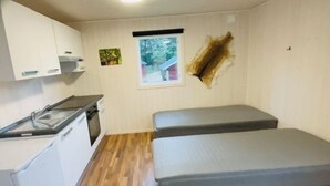 Una habitación compacta con kitchenette, un ventanal pequeño y un estante en la pared.