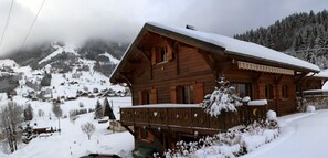 A wooden chalet with a balcony, surrounded by snow-covered mountains.
