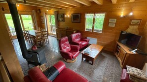 A wooden interior with a sofa, red leather chairs, a television, and a dining area with a table and chairs. - Spacious chalet with WIFI, pets allowed, private garage (Abondance)