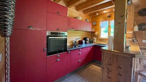 A kitchen with red cabinets, a stainless steel oven, and wooden ceiling beams. - Spacious chalet with WIFI, pets allowed, private garage (Abondance)