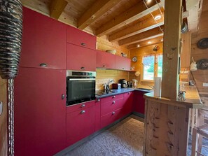 A kitchen with red cabinets, a stainless steel oven, and wooden ceiling beams.