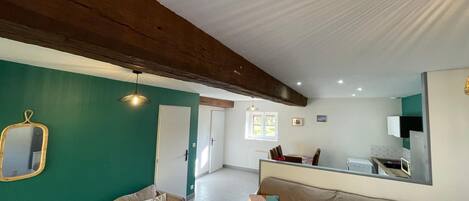 Una habitación con una pared verde, dos sofás, un espejo y una viga de madera en el techo.