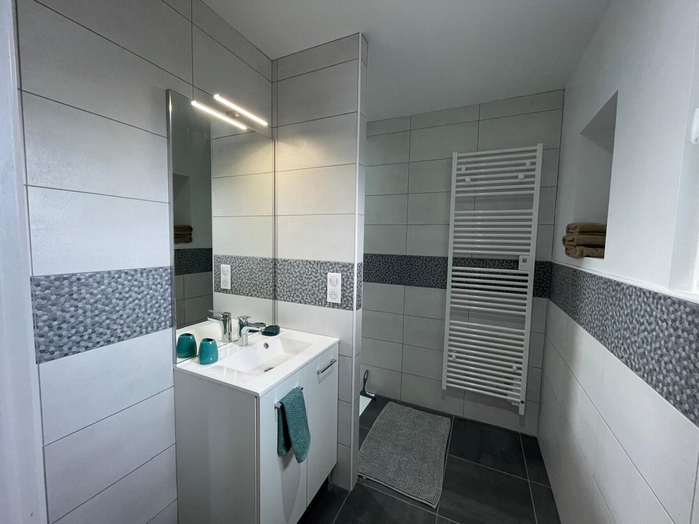 Ein modernes Badezimmer mit weißem Waschbecken, Spiegel und Handtuchhalter.