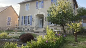 A two-story house with a stone facade, blue shutters, and a central entrance.